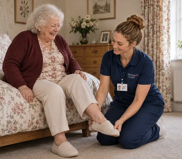 Live-in carer kneeling to help an older woman with her slippers by the bed Live-in carer kneeling to help an older woman with her slippers by the bed